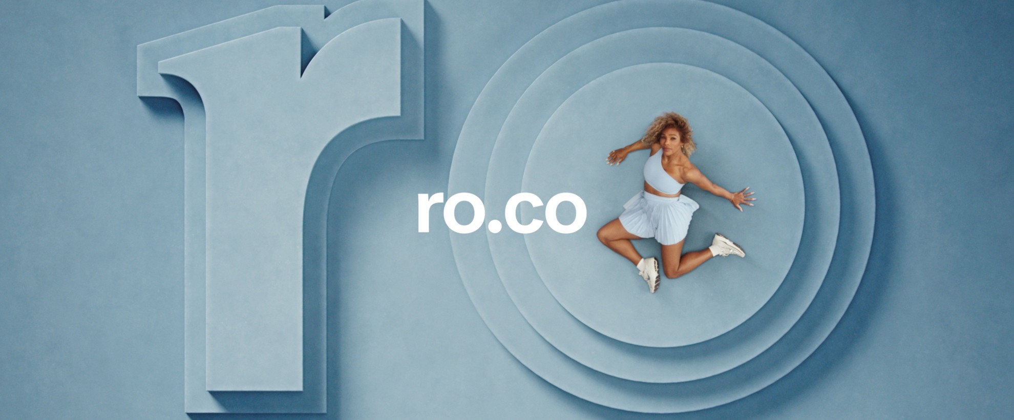 Serena Williams sits on a blue set with set pieces that say ro. She sits on the O