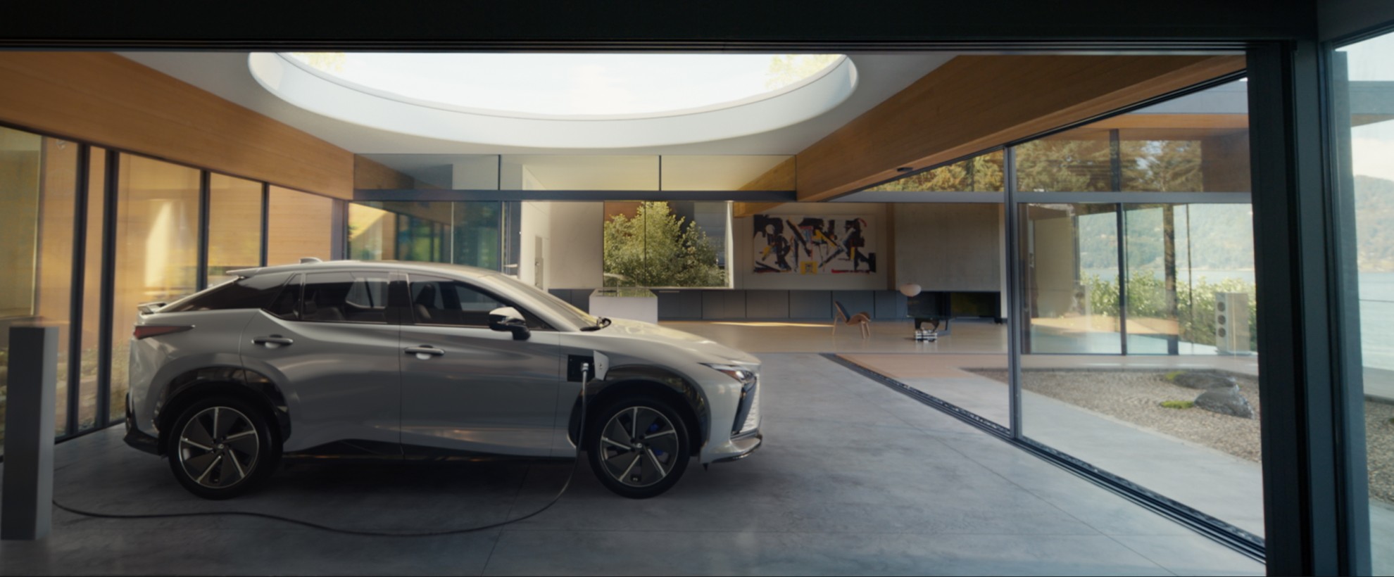 A white electric Lexus SUV charging inside a modern glass-walled home overlooking a serene lakeside landscape