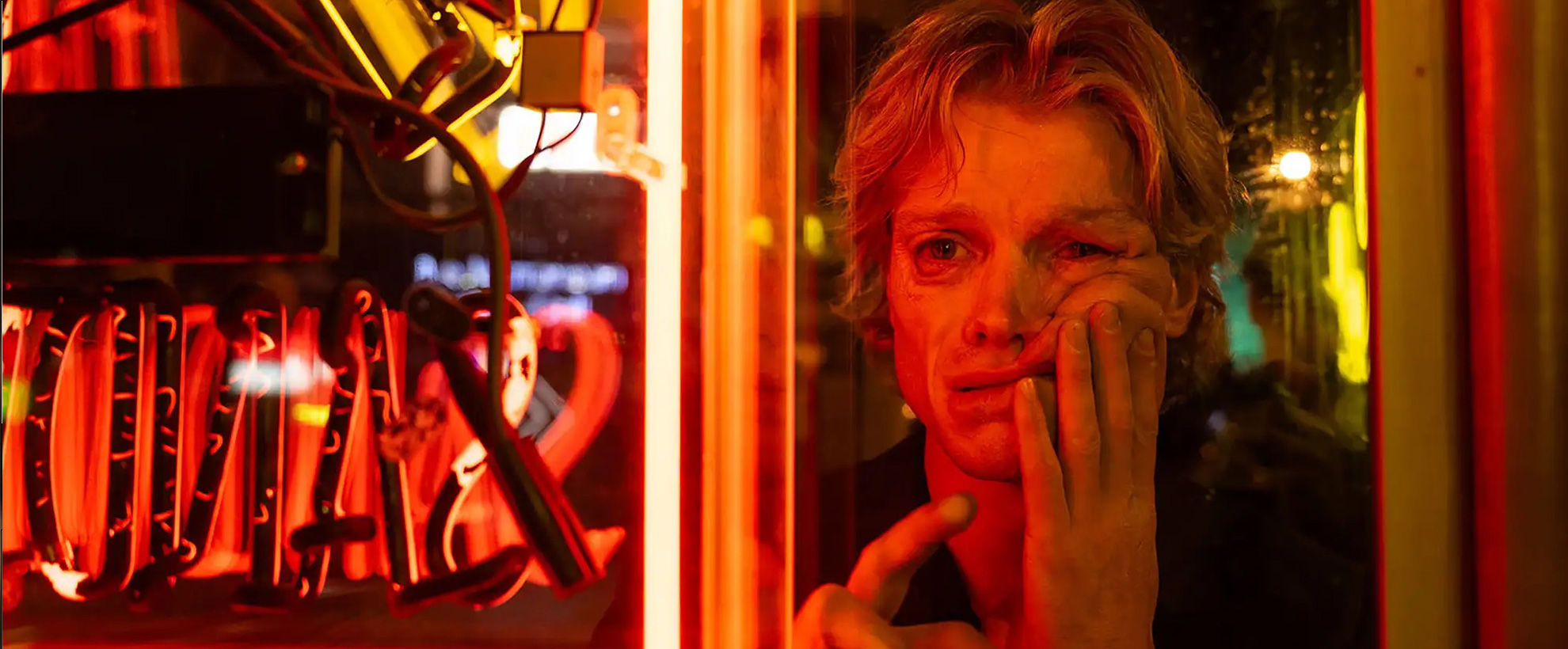 Matt Hagen looks at his reflection in a neon-lit window as his face begins to melt