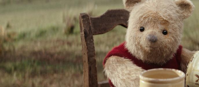 cg animated photorealistic winnie the pooh teddy bear sitting at a table with honey circling his face. there are empty honey pots in front of him