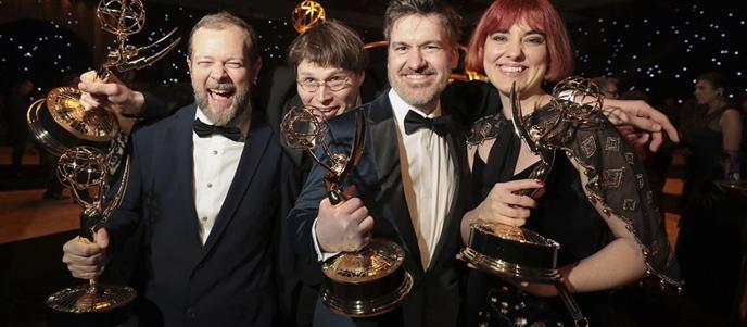 A small group of people in black tie attire, holding Emmy awards