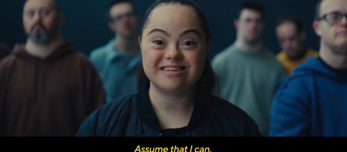 A still from an advert featuring a young woman with Downs syndrome. The caption reads "assume that I can"