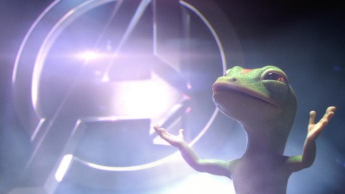 geico gecko mascot with its arms open looking up to the sky with the avengers logo gleaming in the background