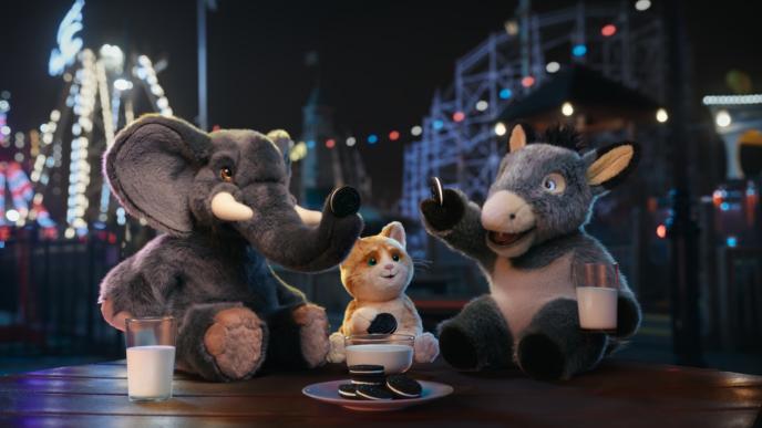 three stuffed animated animals at a fair. an elephant sitting on the left. a cat in the centre holding an oreo cookie. a donkey on the right holding up an oreo cookie and there is a glass of milk right beside it. they are happy