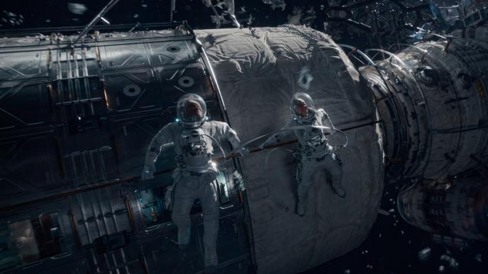 Two astronauts reach for each other outside a spaceship