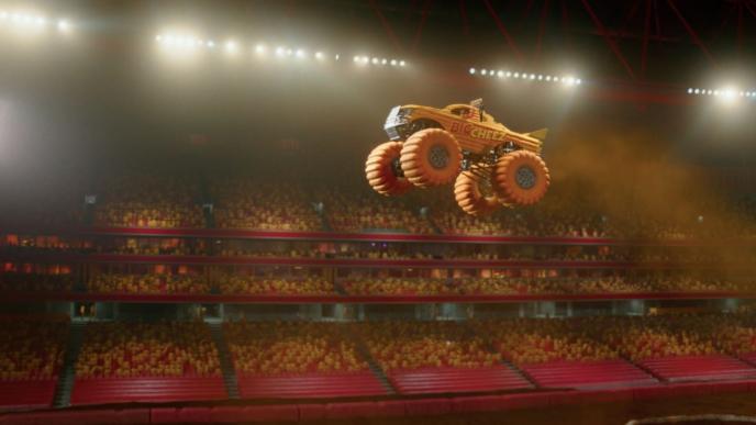 a yellow monster truck mid air with stage lights and spectators in the background