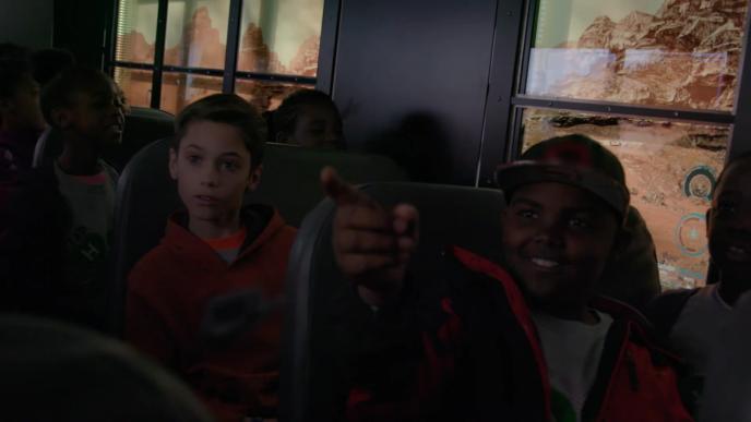 seven children in a school bus with one of them smiling and pointing outside with mars environment in the windows background