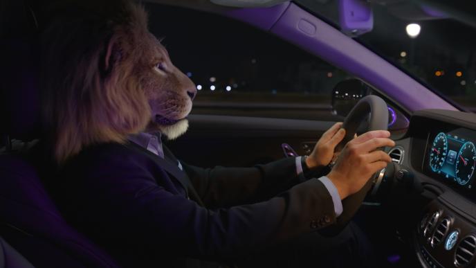 side view of a businessperson with the head of a lion driving a car