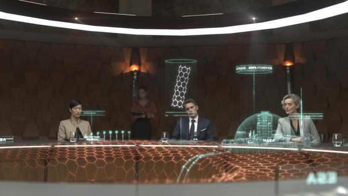 three people sitting around a conference table as one person is standing in the back taking notes. the table has holograms that is projecting nasa infographics