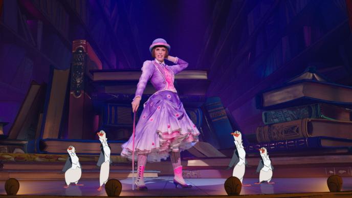 Emily Blunt as Mary Poppins, on stage with cartoon penguins