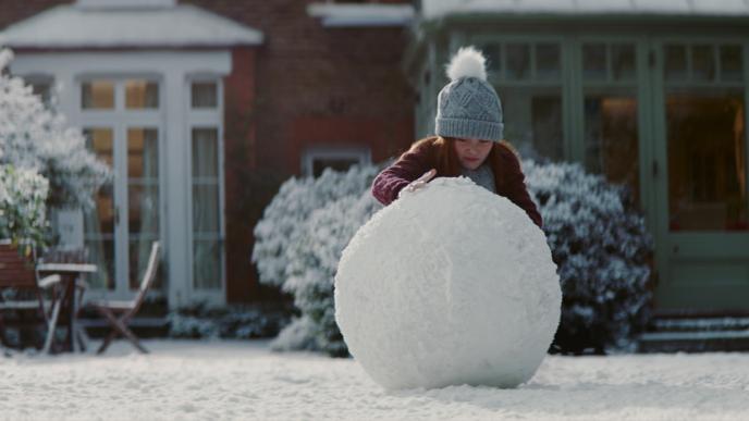 a child rolling a giant snow ball in front of a house