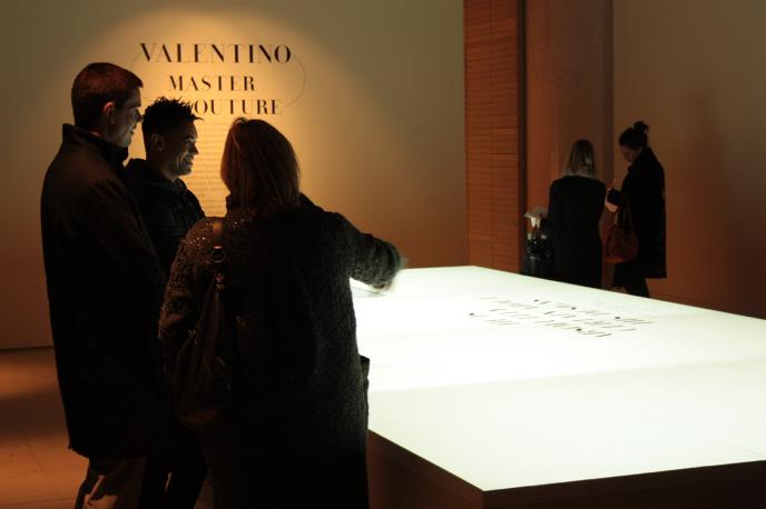 people gathered next to an illuminiscent table at a valentino exhibition