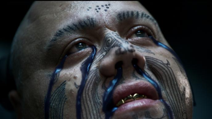 close up face shot of a person with indigenous face tattoos. there is black ink coming out of their eyes and nostrils
