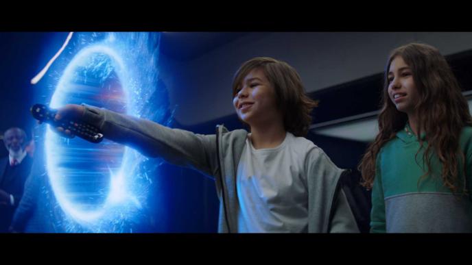 two children standing side by side. one of them is holding a tv remote through a portal
