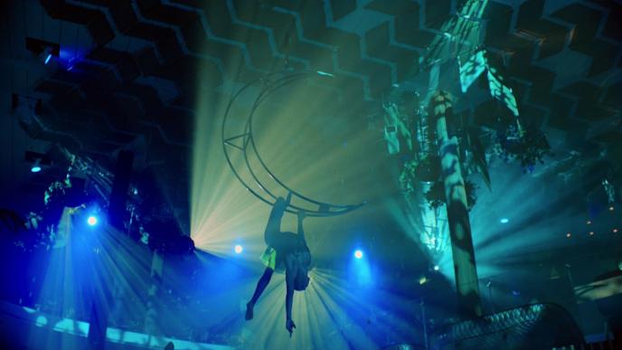 an aerialist suspended in air hanging from a crescent moon shaped trapez