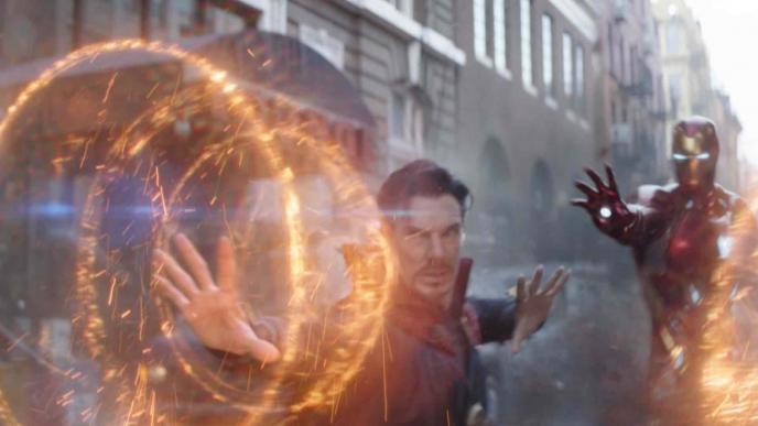doctor strange holding his palms out creating circular sparks by performing black magic as iron man has his palms out in the back