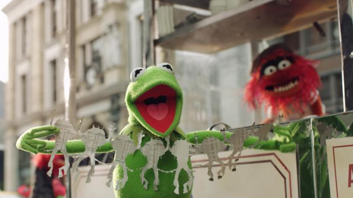 kermit the frog holding up a paper cutting of animal the muppet as animal the muppet stands behind a food stall