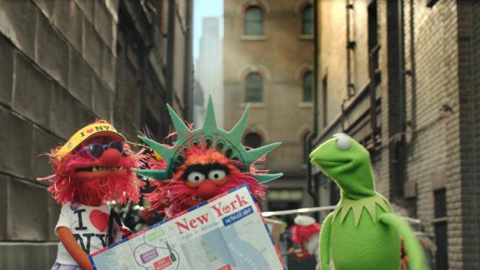 kermit the frog standing next to two red animal muppets wearing new york souvenirs and merch