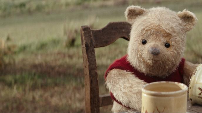 cg animated photorealistic winnie the pooh teddy bear sitting at a table with honey circling his face. there are empty honey pots in front of him