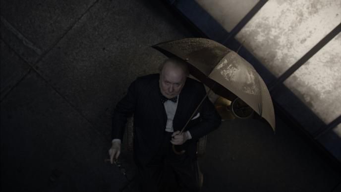 a black and whie image of an aerial shot of winston churchill looking up and holding an umbrella