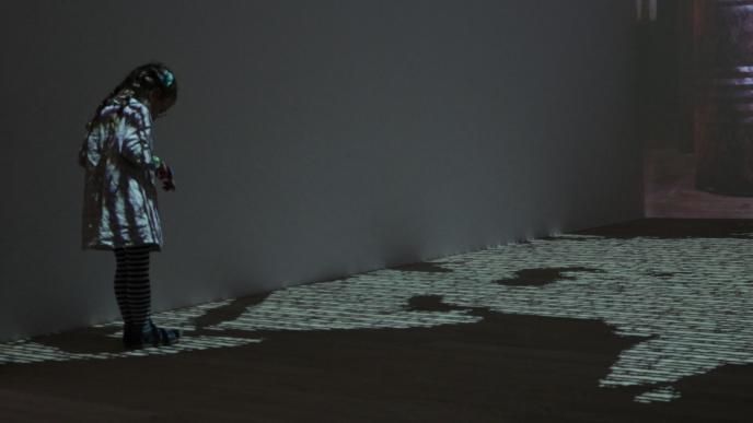 a child looking down at an exhibition that is projected across the walls and floor