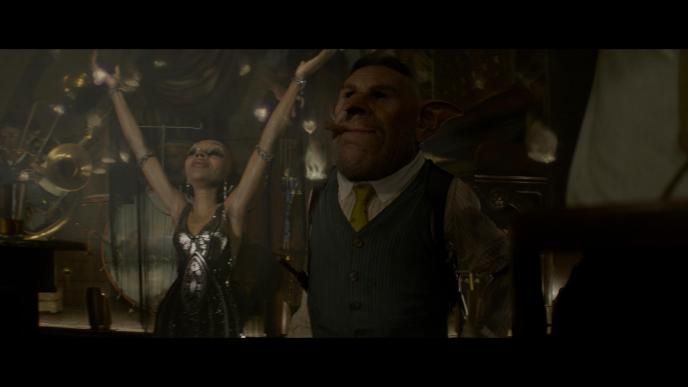 the goblin gnarlak wearing a waist coat shirt and yellow tie standing with a cigar in its mouth as a female goblin wearing a silver detailed dress with her arms up in the air. they are in the blind pig bar