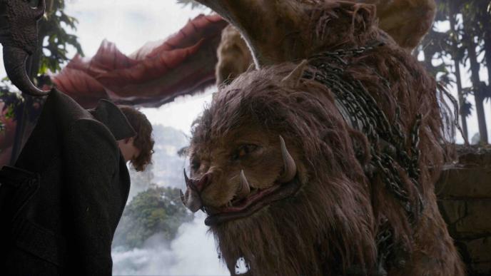 a chained up zouwu beast looking at newt scamander while holding him with its claw