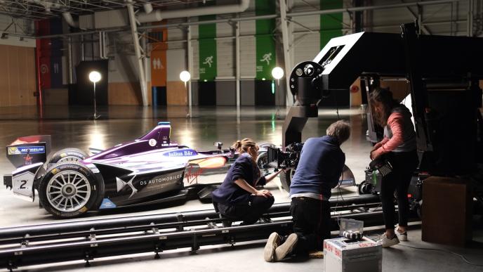 film crew setting up a camera on a slider next to a formula e electric race car