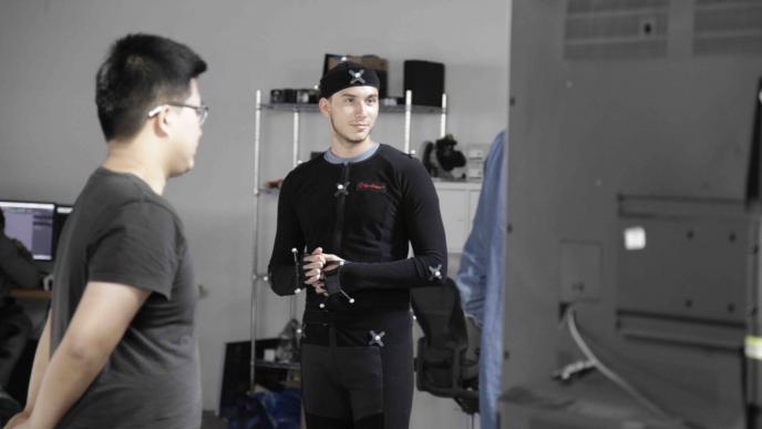 a man wearing a motion capture suit looking into a screen as a film crew stands by