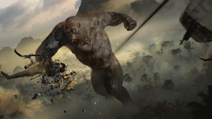 king kong punching and destroying a helicopter as another one approaches it. there is a forest engulfed in smoke