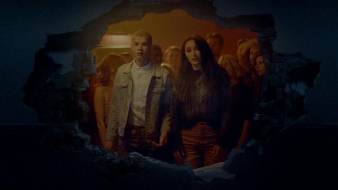 two actors looking through a wall that has been blown. there is a large crowd in the background