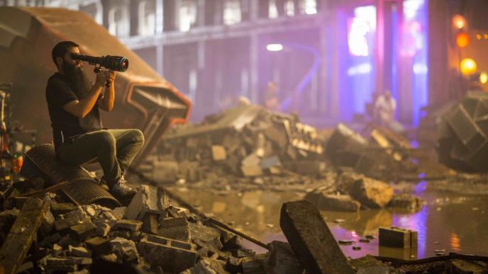 a cameraman sitting on rubble recording a scene