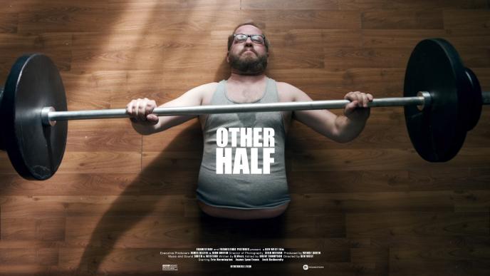 a man with only a torso doing a bench press with a barbell on laminate flooring. 'other half' text is in the centre of the image with credits at the bottom