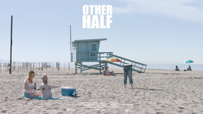 a man's torso sitting next to a woman at a beach as the man's legs stand nearby