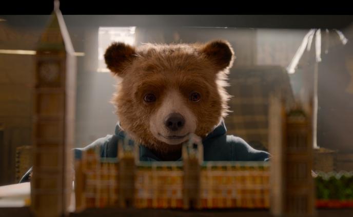 paddington bear looking at a paper mache of big ben clock tower and parliament