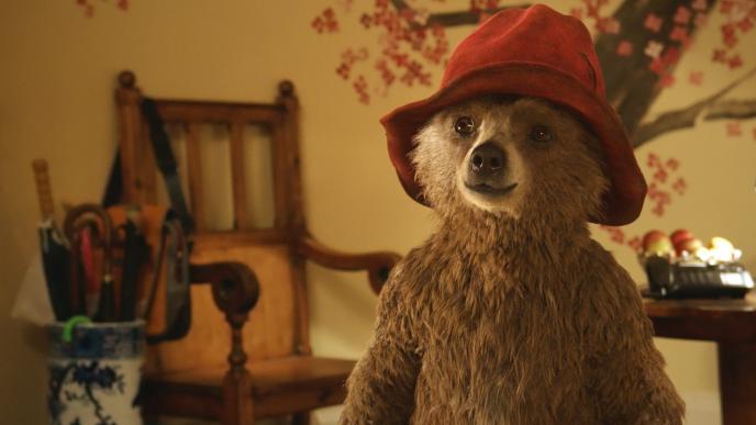 cg animated photorealistic paddington bear wearing a red hat smiling while looking to the left. paddington bear is standing in a living room