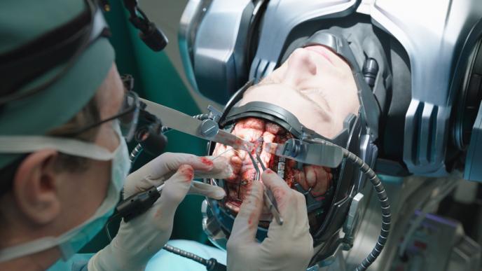 robocop murphy at a surgery table with his brain exposed as a brain surgeon operates on it