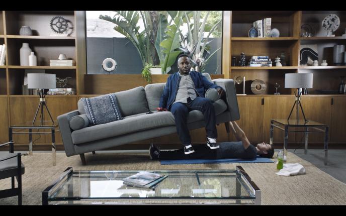 actor tom holland doing a bench press with a sofa while comedian hannibal buress is sitting