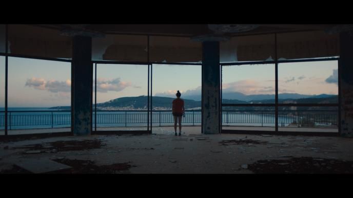 back perspective of a person standing by large balcony windows looking out to the sea and mountains