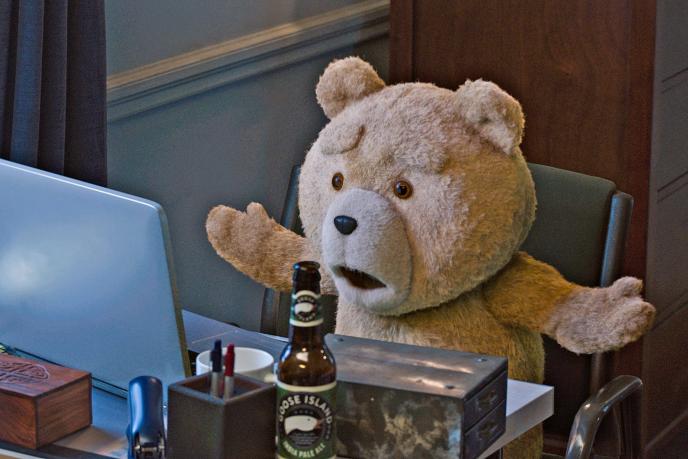 animated life sized teddy bear ted sitting at a desk looking at a laptop with his arms up