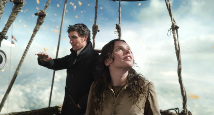 actors eddie redmayne and felicity jones from the aeronauts standing in a hot air balloon in the sky surrounded by clouds and butterflies