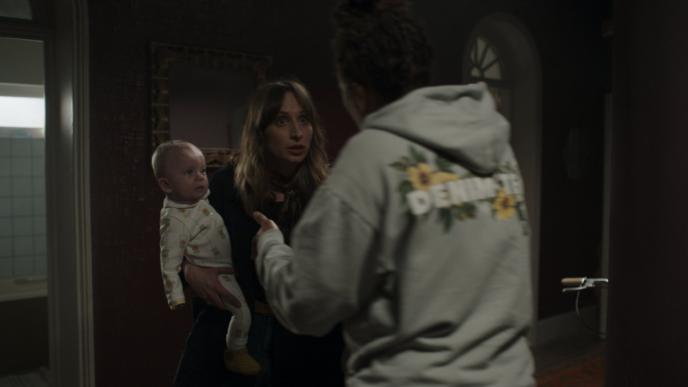 a woman holding a baby in her arms talking to someone at her front door