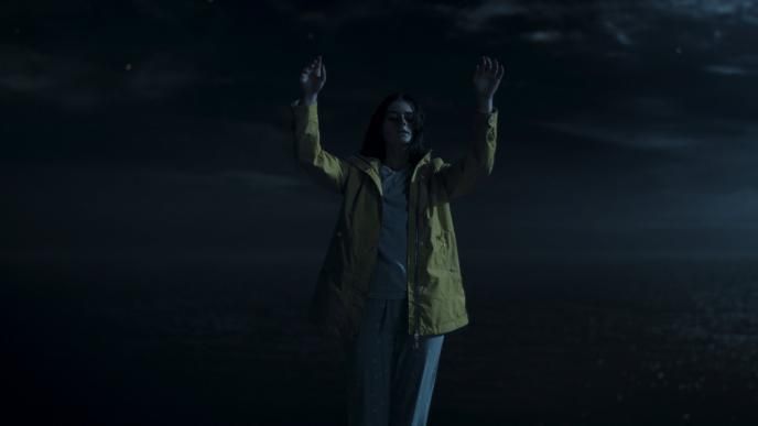 a woman standing on top of a cliff looking down while holding her hands up