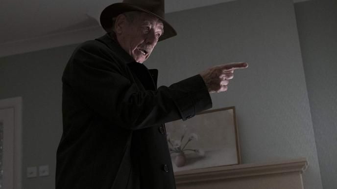 actor ian mckellen wearing a black jacket and a fedora pointing to the right