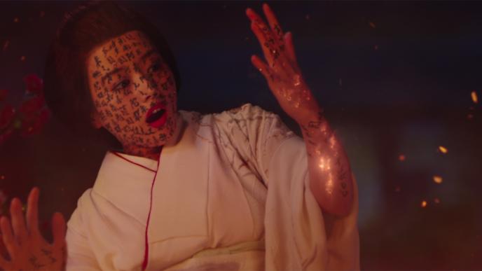 a geisha wearing white robes looking at her hands in shock as kanji characters appear on her face and arms