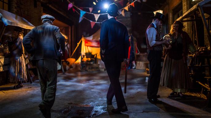 back view of two people walking through a victorian era london street film set