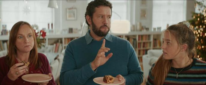 parents shushing their teenage daughter as they eat pork pies and she looks at them with a surprised expression