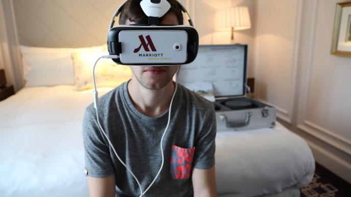 a man sitting on the edge of a bed in a hotel room wearing a samsung branded marriott vroom service vr headset