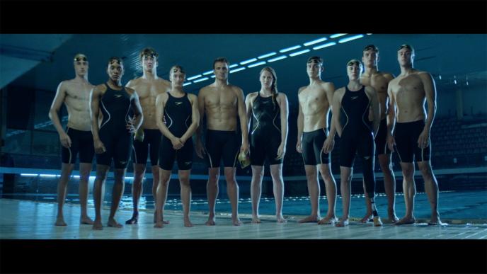 a group of ten professional swimmers standing in front of a swimming pool with their swimming goggles on their foreheads