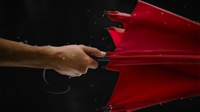 close up of a hand holding a red umbrella. there are rain droplets